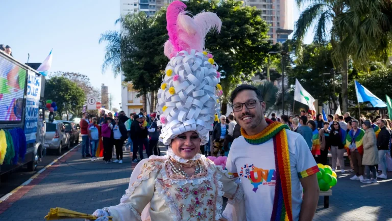 At the gathering, the drag queen with a sculpted wig poses next to a participant in a rainbow scarf.