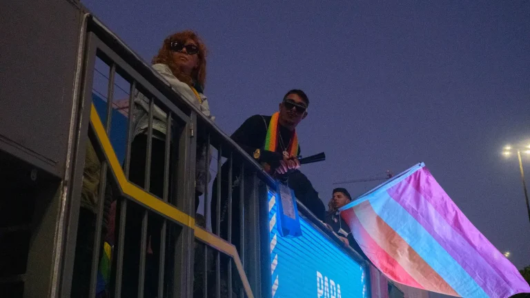 A trans flag waves against the blue night sky.