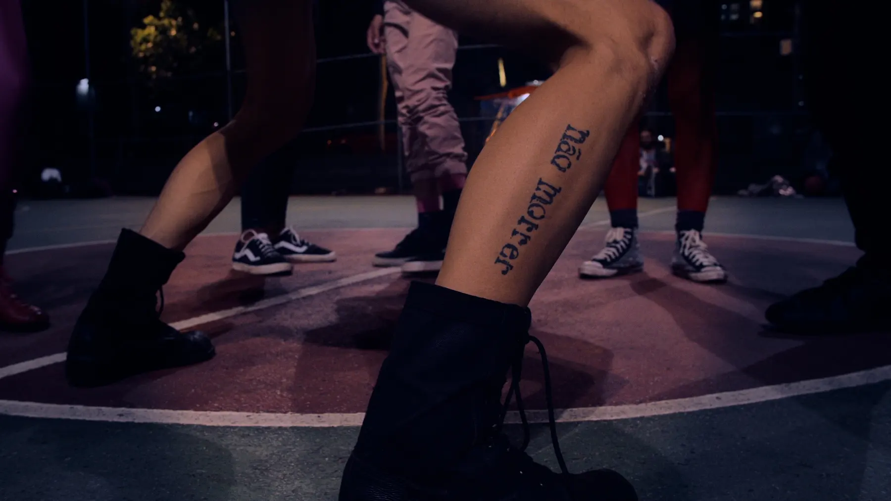 Pernas com botas e tênis dançando vogue numa quadra de basquete à noite, em cena do documentário Basquete das Excluídas