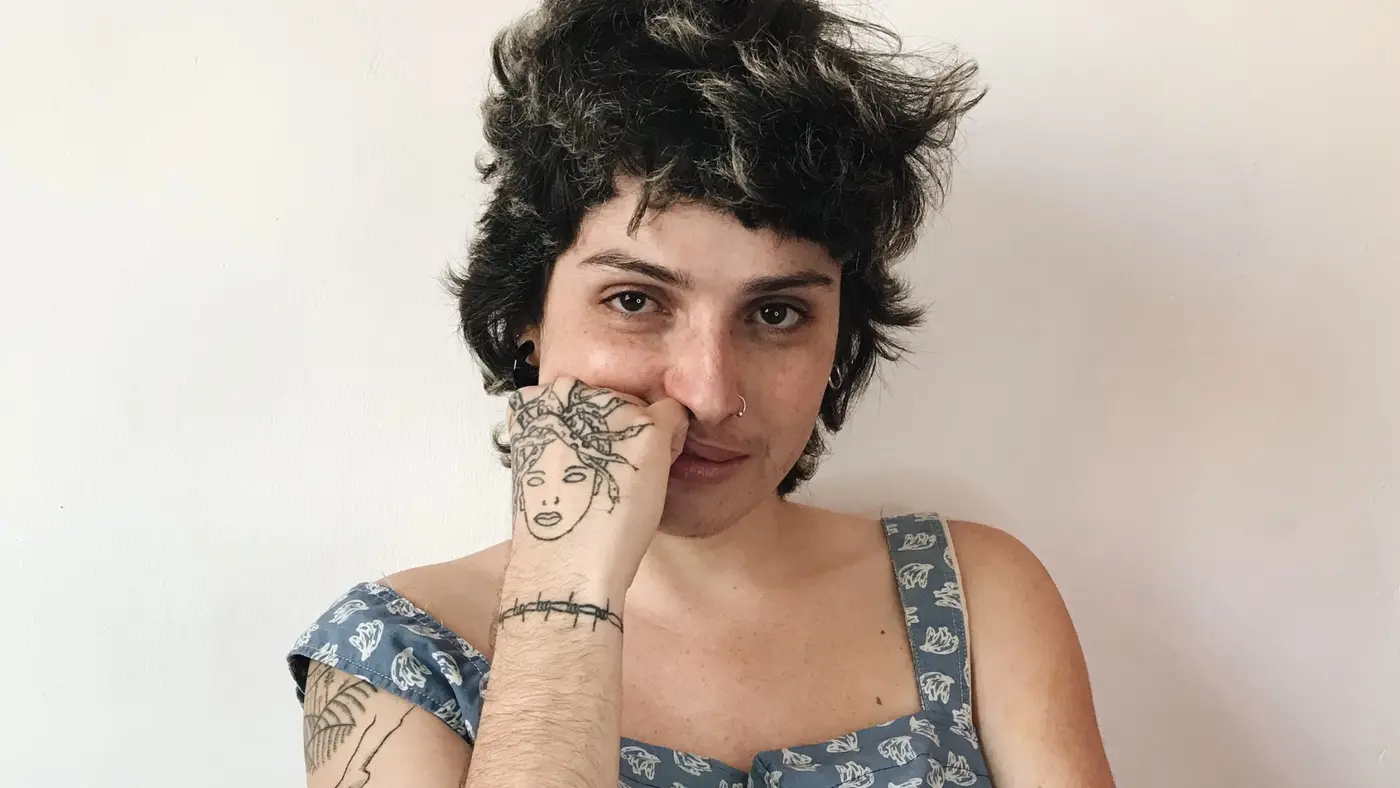 Retrato da poeta Keythe Tavares, de cabelo curto, com a mão tatuada apoiada no rosto