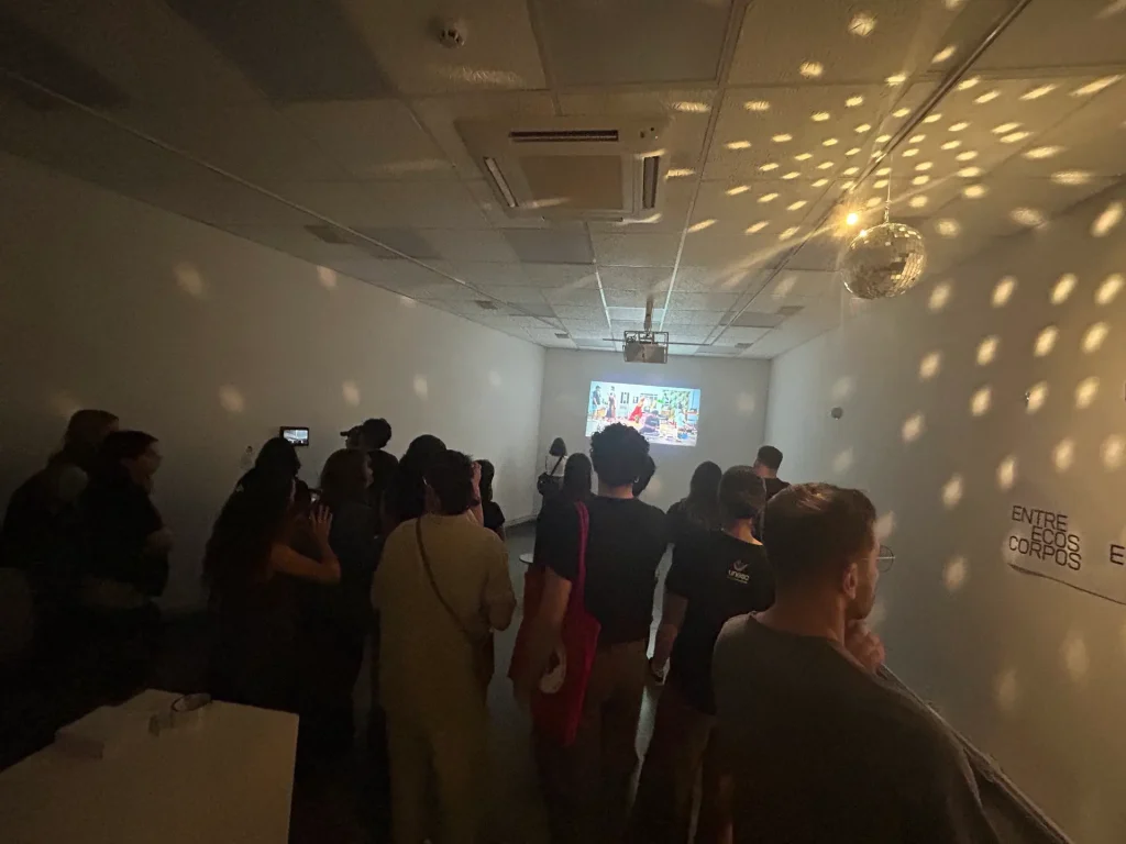 Público de costas assistindo à projeção, com o teto coberto de reflexos