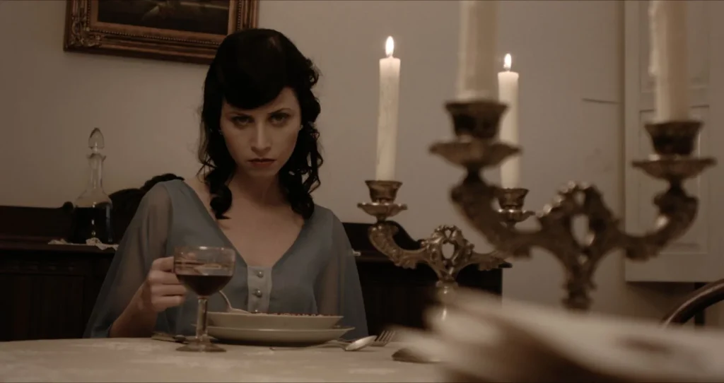 Preto Pálido: Analu à mesa de jantar, com taça de vinho e candelabro