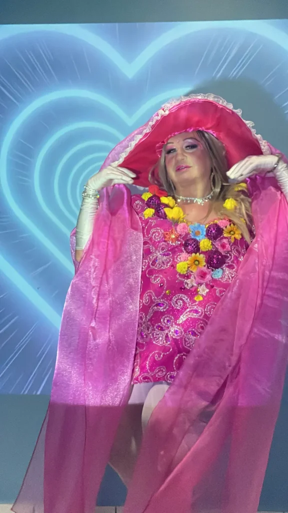 A drag performa diante da projeção de um coração neon